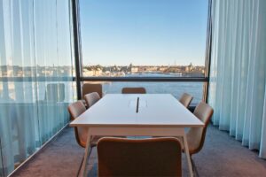 Konferensrum med vitt bord, bruna stolar och utsikt över stad och vatten