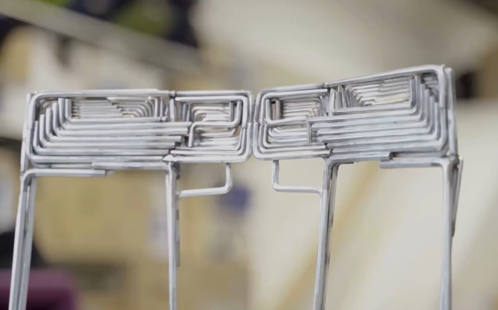 Stol med ryggstöd av böjda metallstänger i geometriskt, industriellt mönster.
