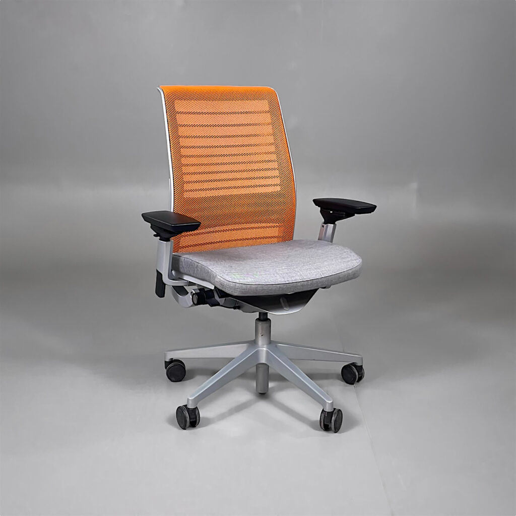 En kontorsstol med orange nätrygg, grå sits och hjulförsett underrede.