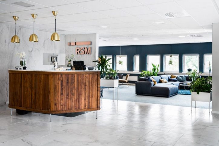 Reception med trädisk, marmorskiva, hänglampor, RSM-logga och lounge med soffor och växter.