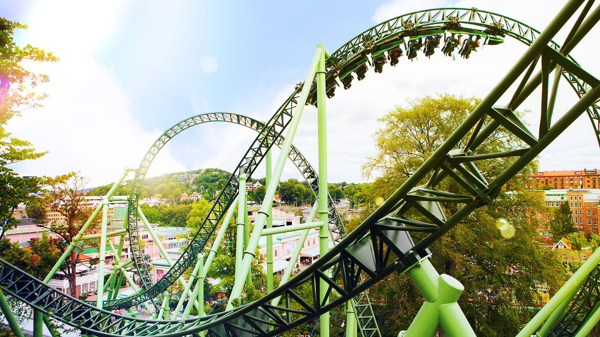 Grön berg-och-dalbana i fartfyllt nöjesfält med blå himmel.