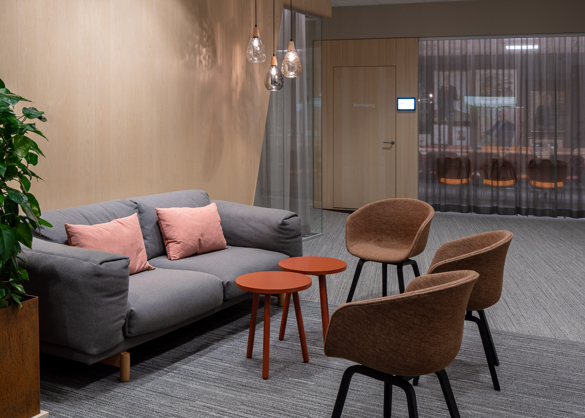 Väntrum med grå soffa, bruna stolar, orange bord och trävägg med lampor