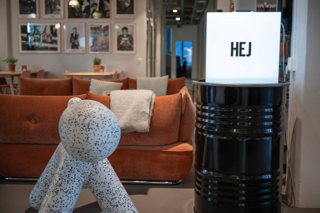 Välkomnande lounge med orange soffa, designmöbel och ljuslåda med texten "HEJ".