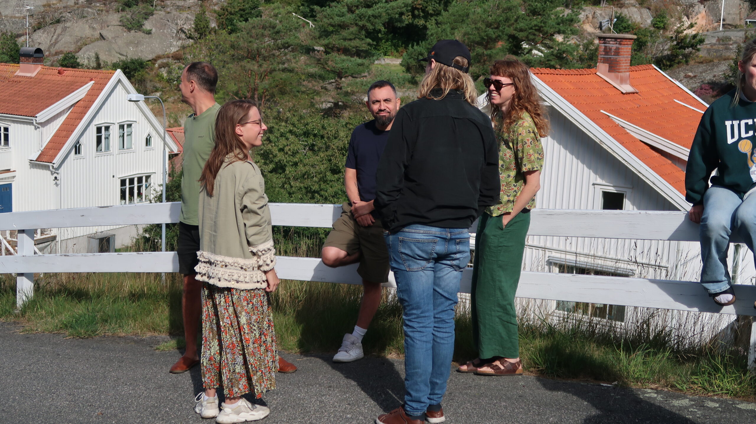 Fyra personer samtalar utomhus vid vitt staket.