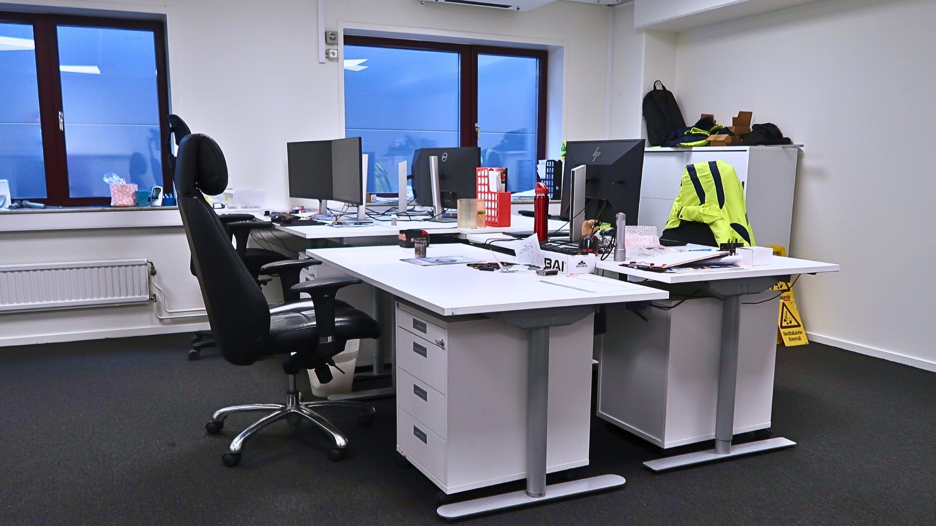 Fyra kontorsplatser med datorer, kontorsstolar och fönster.