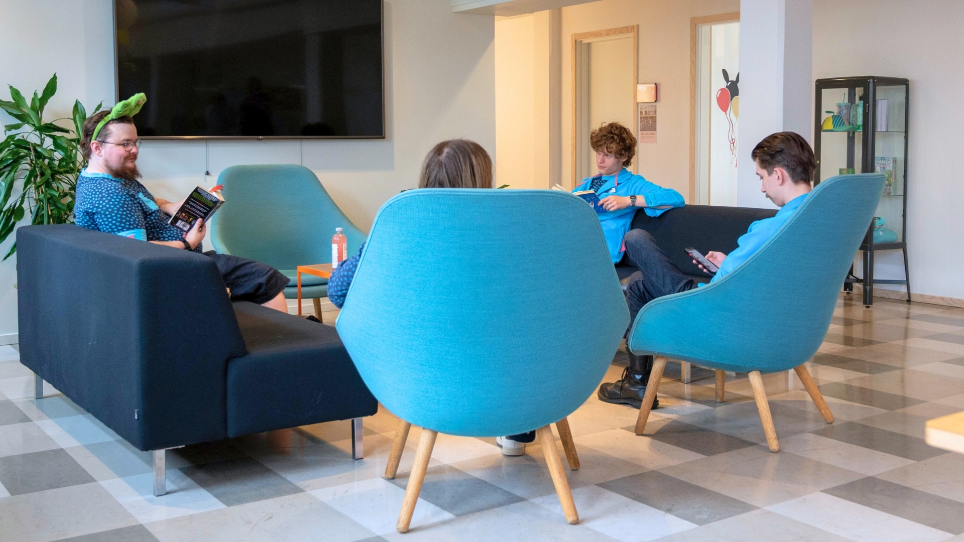 Fyra personer i lounge med soffor, teknik och växter i en modern kontorsmiljö.