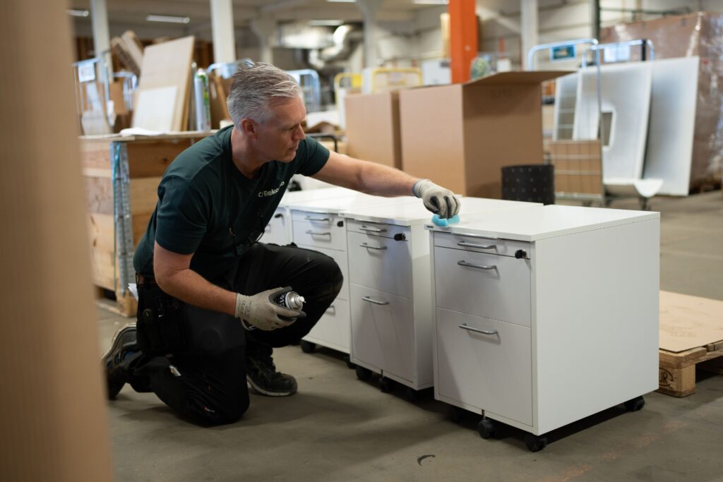 Person rengör vita förvaringsskåp med duk i en industriell miljö med kartonger och material.