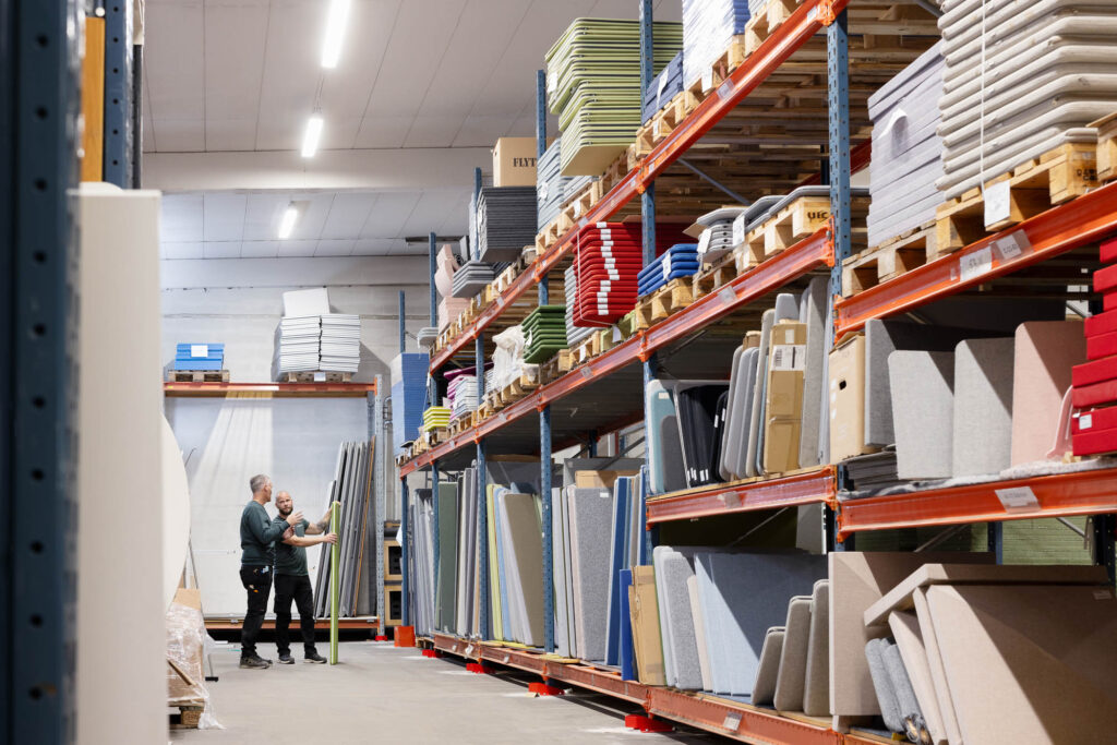 Två personer i ett lager med höga hyllor fyllda med bordsväggar.