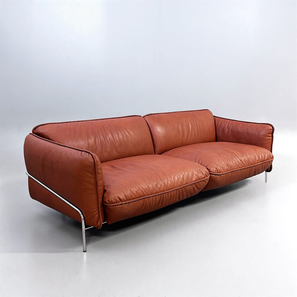 En modern soffa i konjaksfärgat läder med tunna metallben.