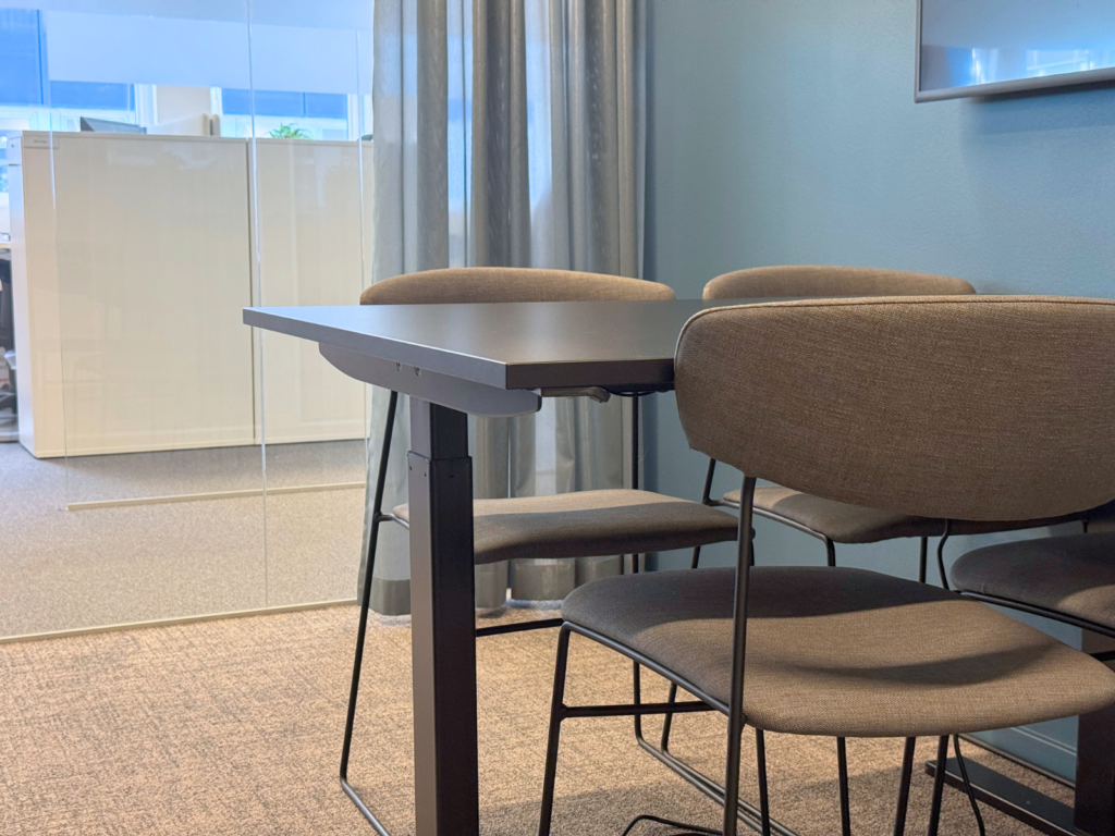 Litet mötesrum med bord, stolar, glasvägg och gardin i modern kontorsmiljö