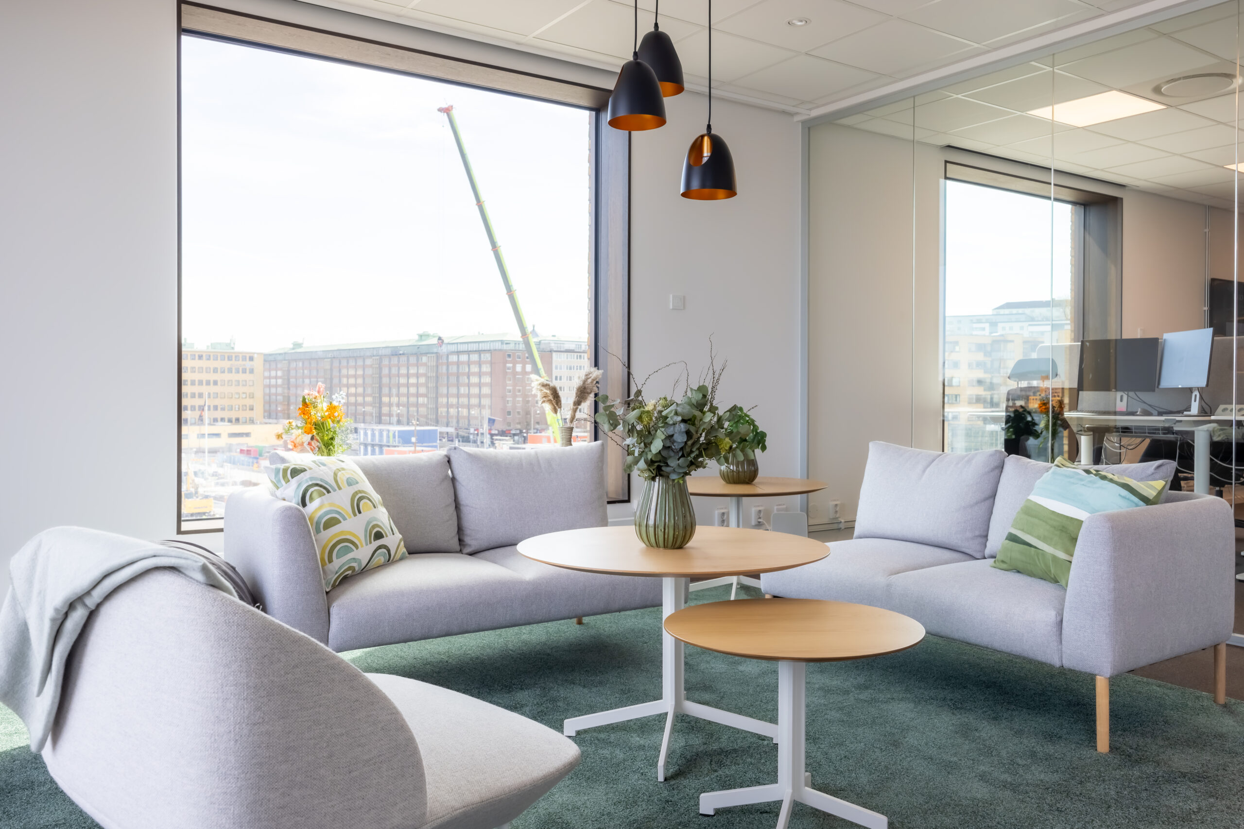 Lounge med en grå soffa och matchande fåtölj samt runda bord placerade på en matta vid fönster.